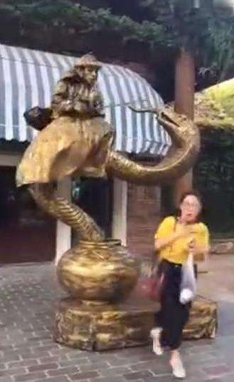 美女跟铜像合影，铜像却突然流出了水，美女转头一看被吓了一跳